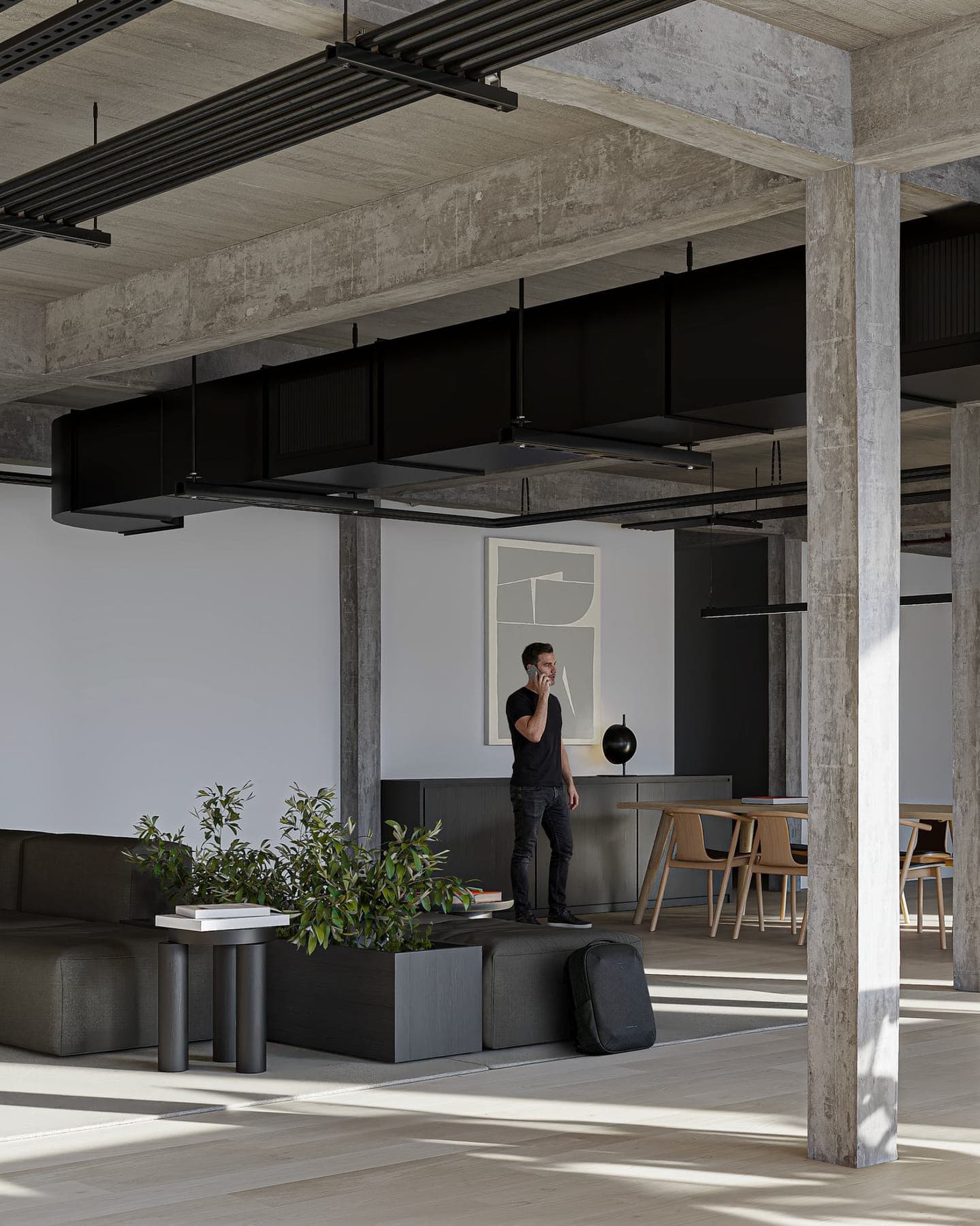 Área de estar del coworking con sillones, mesa de reuniones de madera y vegetación entre columnas de hormigón